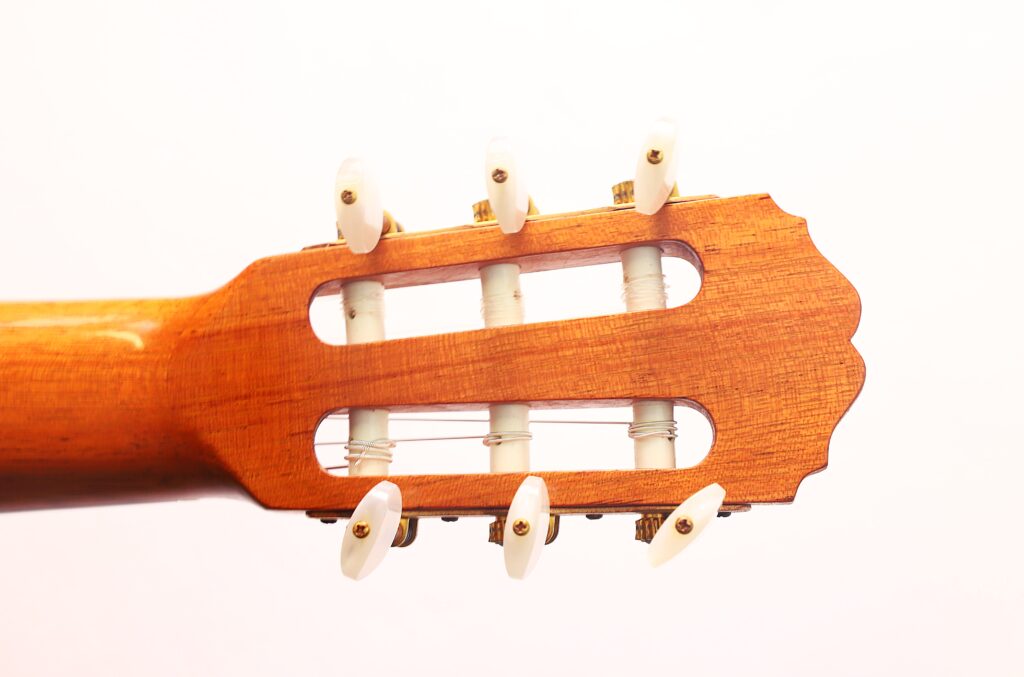 Nahaufnahme der Kopfplatte und der Stimmwirbel der Antonio Aparicio Mod. Master Klassische Gitarre, mit hellbraunem Holz und weißen Stimmknöpfen vor einem schlichten weißen Hintergrund. Nahaufnahme der Kopfplatte und der Stimmwirbel der Antonio Aparicio Mod. Master Klassische Gitarre, mit hellbraunem Holz und weißen Stimmknöpfen vor einem schlichten weißen Hintergrund.