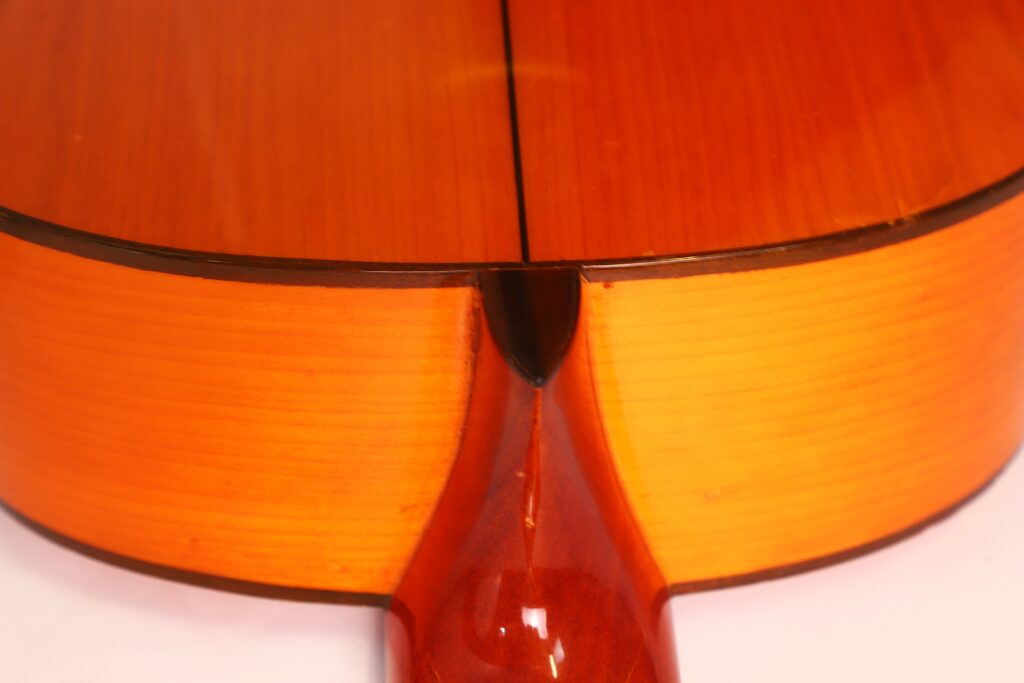 Nahaufnahme des Halsgelenks einer Conde Hermanos 1990 FelipeV N2 Flamenco-Gitarre. Hervorzuheben sind die glänzende orange-braune Oberfläche und die feine Holzmaserung. Nahaufnahme des Halsgelenks einer Conde Hermanos 1990 FelipeV N2 Flamenco-Gitarre. Hervorzuheben sind die glänzende orange-braune Oberfläche und die feine Holzmaserung.