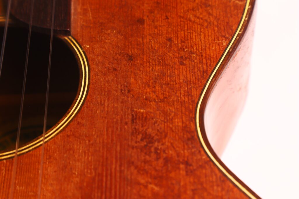 Nahaufnahme des Korpus der Braun & Hauser 1905 Klassische Gitarre mit Schallloch, Holzmaserung und Saiten. Die warme Beleuchtung unterstreicht die eleganten Rundungen und das feine Finish der Gitarre. Nahaufnahme des Korpus der Braun & Hauser 1905 Klassische Gitarre mit Schallloch, Holzmaserung und Saiten. Die warme Beleuchtung unterstreicht die eleganten Rundungen und das feine Finish der Gitarre.