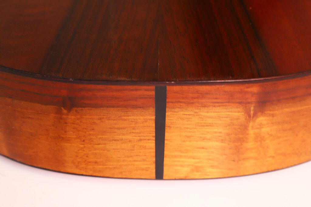 Nahaufnahme der Andres Marin 1890 Klassische Gitarre, die den Kontrast zwischen dem dunkleren Holzboden und der helleren Holzseite hervorhebt, die durch eine dünne schwarze Naht getrennt sind. Nahaufnahme der Andres Marin 1890 Klassische Gitarre, die den Kontrast zwischen dem dunkleren Holzboden und der helleren Holzseite hervorhebt, die durch eine dünne schwarze Naht getrennt sind.