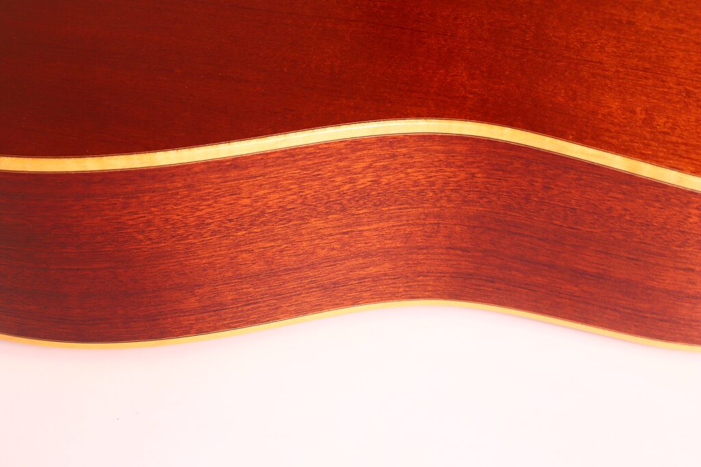 Nahaufnahme der Seite der Lakewood D-14-12 Cut 2005 Akustik Gitarre, die die Holzmaserung, die geschwungene Kante und die helle Zierleiste vor einem weißen Hintergrund hervorhebt. Nahaufnahme der Seite der Lakewood D-14-12 Cut 2005 Akustik Gitarre, die die Holzmaserung, die geschwungene Kante und die helle Zierleiste vor einem weißen Hintergrund hervorhebt.