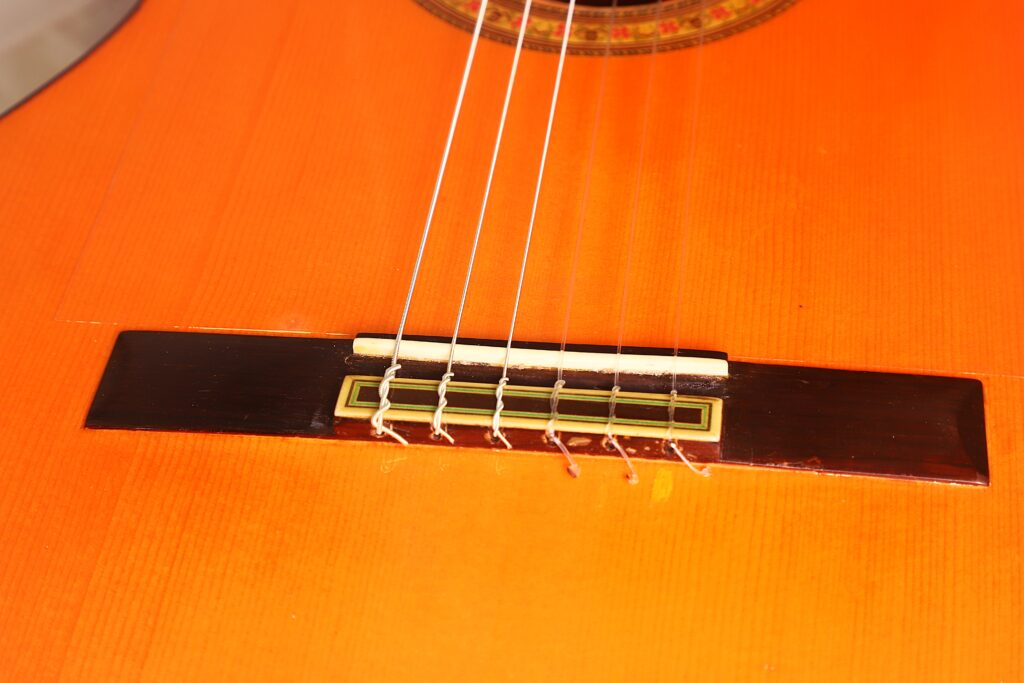 Nahaufnahme des Stegs, der Saiten, des Holzkorpus, des Sattels und des unteren Schalllochs einer José M Palmero 2023 Flamenco-Gitarre. Nahaufnahme des Stegs, der Saiten, des Holzkorpus, des Sattels und des unteren Schalllochs einer José M Palmero 2023 Flamenco-Gitarre.
