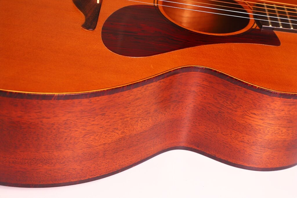 Nahaufnahme der Lowden S-5 Akustikgitarre, die den Holzkorpus, die detaillierte Maserung, die Saiten und das Schlagbrett vor einem weißen Hintergrund hervorhebt. Nahaufnahme der Lowden S-5 Akustikgitarre, die den Holzkorpus, die detaillierte Maserung, die Saiten und das Schlagbrett vor einem weißen Hintergrund hervorhebt.