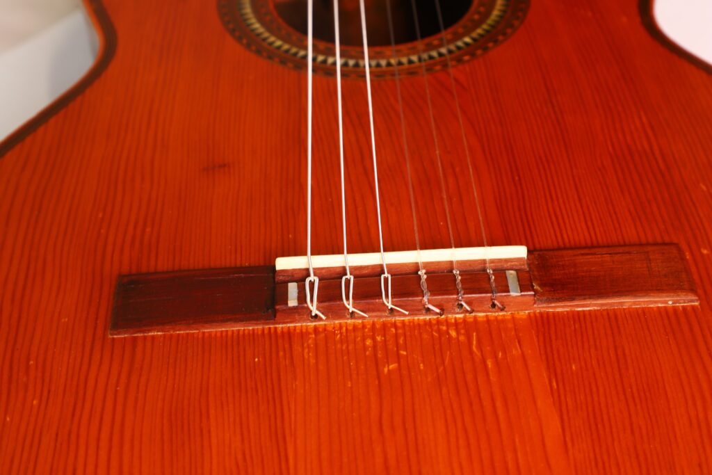 Nahaufnahme der Saiten und des Stegs einer Andres Marin 1900 Klassische Gitarre, die die Holzmaserung und die feine Handwerkskunst des Instrumentenkörpers hervorhebt. Nahaufnahme der Saiten und des Stegs einer Andres Marin 1900 Klassische Gitarre, die die Holzmaserung und die feine Handwerkskunst des Instrumentenkörpers hervorhebt.