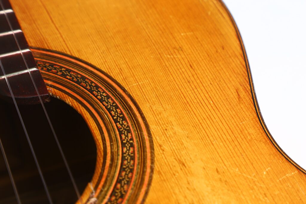 Nahaufnahme der klassischen Gitarre „Jose Ramirez I 1921“ mit Fokus auf das Schallloch, die Saiten und die kunstvoll verzierte Rosette auf dem warm lackierten Holzkorpus. Nahaufnahme der klassischen Gitarre „Jose Ramirez I 1921“ mit Fokus auf das Schallloch, die Saiten und die kunstvoll verzierte Rosette auf dem warm lackierten Holzkorpus.