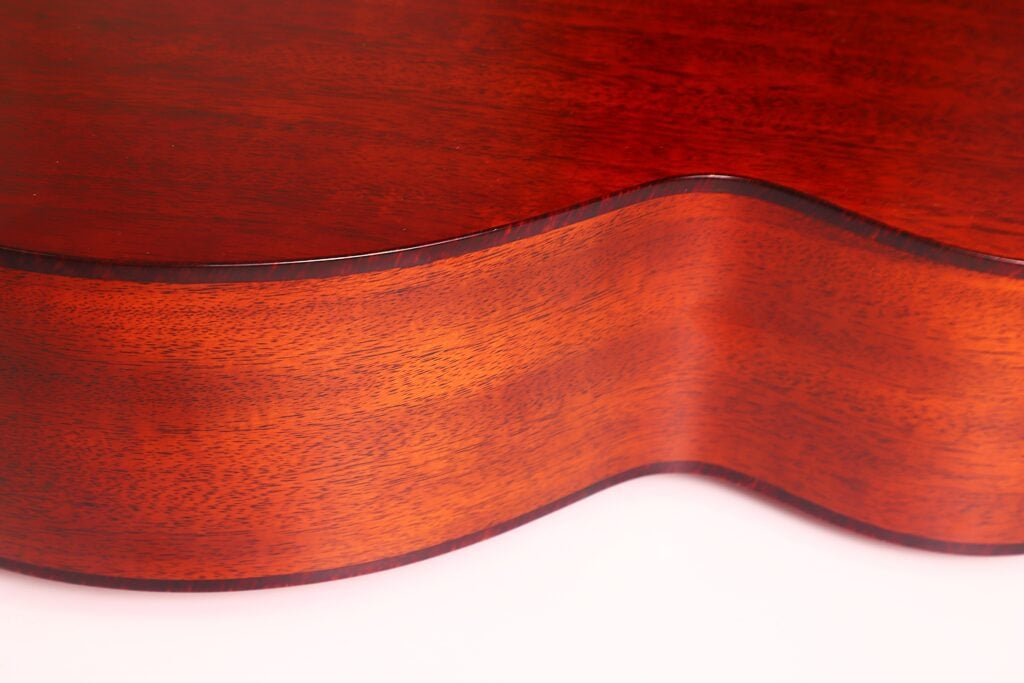 Nahaufnahme der gewölbten, polierten Holzseite einer Lowden S-5 Akustik Gitarre vor weißem Hintergrund, wobei die Holzmaserung und die satte rotbraune Farbe hervorgehoben werden. Nahaufnahme der gewölbten, polierten Holzseite einer Lowden S-5 Akustik Gitarre vor weißem Hintergrund, wobei die Holzmaserung und die satte rotbraune Farbe hervorgehoben werden.