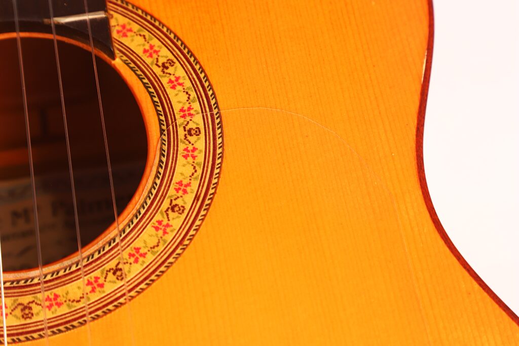 Nahaufnahme des Korpus der José M Palmero 2023 Flamenco-Gitarre, die das Schallloch mit seiner dekorativen Rosette sowie einen Teil der Holzdecke zeigt, auf der ein Riss zu erkennen ist. Nahaufnahme des Korpus der José M Palmero 2023 Flamenco-Gitarre, die das Schallloch mit seiner dekorativen Rosette sowie einen Teil der Holzdecke zeigt, auf der ein Riss zu erkennen ist.