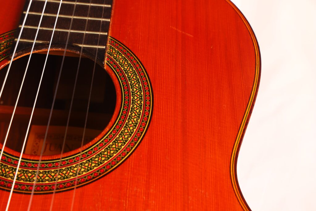 Nahaufnahme einer Juan Estruch Chet Atkins Yellow Label Klassische Gitarre aus dem Jahr 1976, die einen Teil des Schalllochs, das aufwendige Rosettenmuster, die Saiten und die glänzende Holzoberfläche des Korpus vor weißem Hintergrund zeigt. Nahaufnahme einer Juan Estruch Chet Atkins Yellow Label Klassische Gitarre aus dem Jahr 1976, die einen Teil des Schalllochs, das aufwendige Rosettenmuster, die Saiten und die glänzende Holzoberfläche des Korpus vor weißem Hintergrund zeigt.