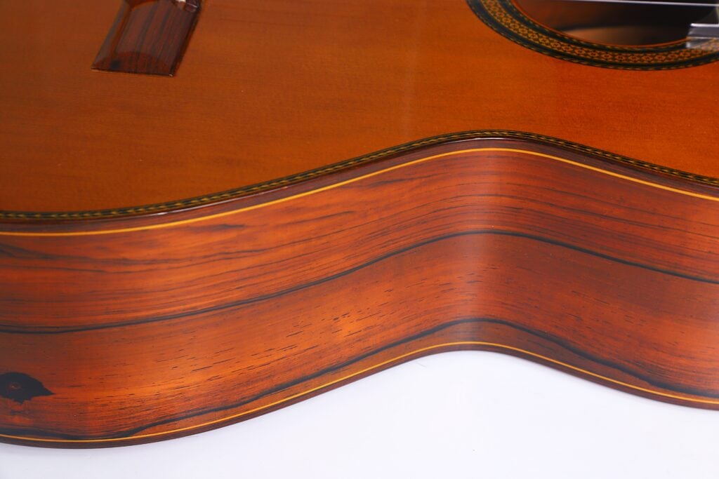 Nahaufnahme der Seite und Oberseite einer „Doble Tapa Klassische Gitarre“ von Manuel Contreras aus dem Jahr 1981, die die Holzmaserung, die glatte Oberfläche und die hochwertige Verarbeitung hervorhebt. Nahaufnahme der Seite und Oberseite einer „Doble Tapa Klassische Gitarre“ von Manuel Contreras aus dem Jahr 1981, die die Holzmaserung, die glatte Oberfläche und die hochwertige Verarbeitung hervorhebt.