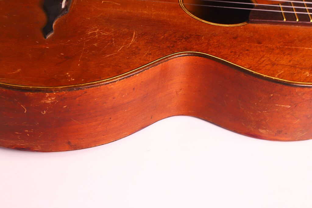 Nahaufnahme des alten Holzkorpus der Braun & Hauser 1905 Klassische Gitarre mit Kratzern und Abnutzungserscheinungen an der gewölbten Kante vor weißem Hintergrund. Nahaufnahme des alten Holzkorpus der Braun & Hauser 1905 Klassische Gitarre mit Kratzern und Abnutzungserscheinungen an der gewölbten Kante vor weißem Hintergrund.