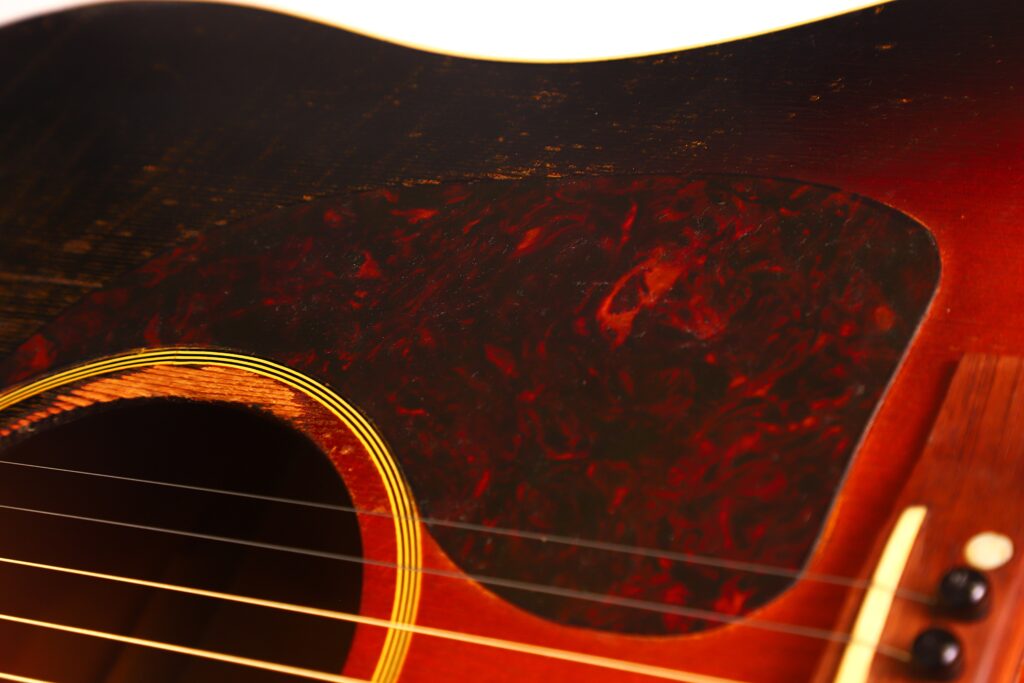 Nahaufnahme einer Gibson J-45 Banner 1944 Akustik Gitarre, die das Schallloch, das marmorierte Schlagbrett, die Saiten und einen Teil des abgenutzten Holzkörpers zeigt. Nahaufnahme einer Gibson J-45 Banner 1944 Akustik Gitarre, die das Schallloch, das marmorierte Schlagbrett, die Saiten und einen Teil des abgenutzten Holzkörpers zeigt.