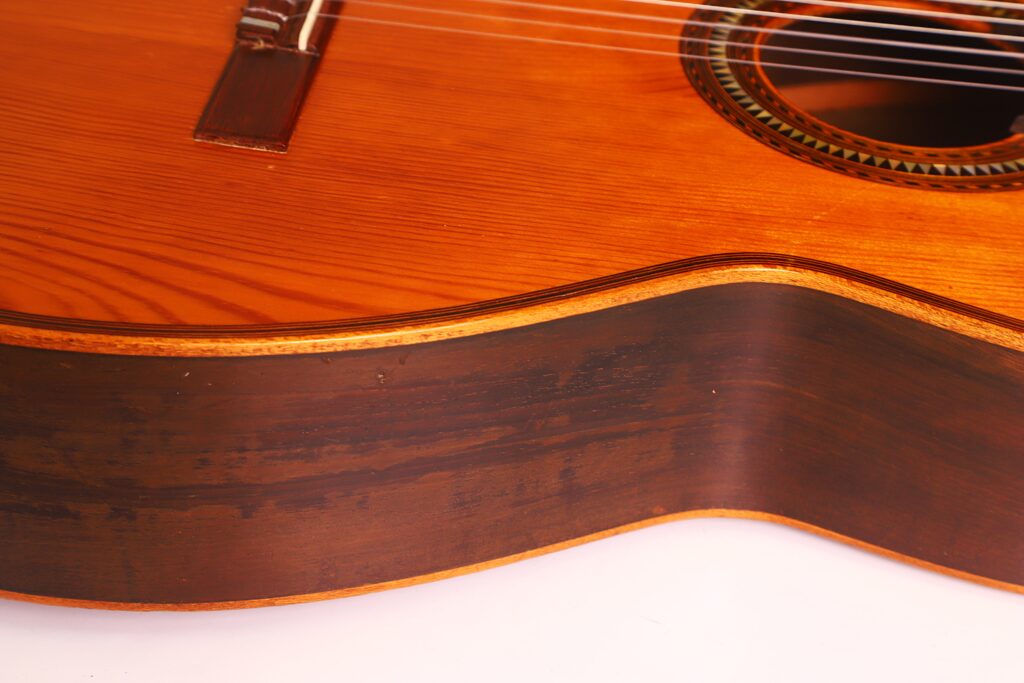 Nahaufnahme des Korpus der Andres Marin 1900 Klassische Gitarre. Hervorzuheben sind die Holzmaserung, die dekorative Schalllocheinlage und der Kontrast zwischen der hellen Decke und den dunklen Seiten. Nahaufnahme des Korpus der Andres Marin 1900 Klassische Gitarre. Hervorzuheben sind die Holzmaserung, die dekorative Schalllocheinlage und der Kontrast zwischen der hellen Decke und den dunklen Seiten.