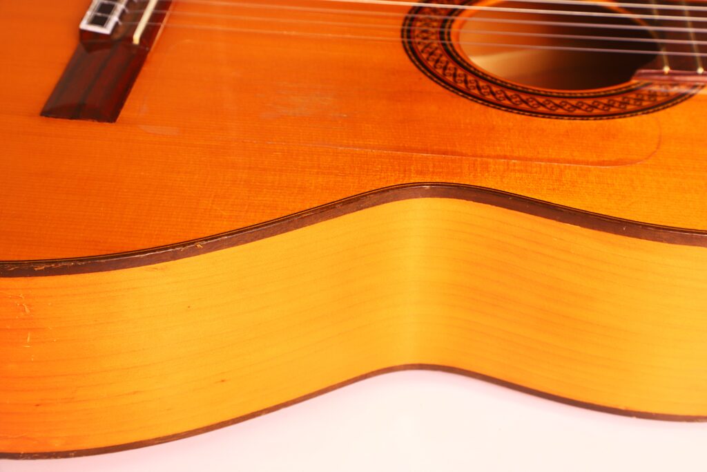 Nahaufnahme des Korpus der Conde Hermanos 1990 FelipeV N2 Flamenco-Gitarre, mit Schallloch, Saiten und Holzmaserung auf weißem Hintergrund. Nahaufnahme des Korpus der Conde Hermanos 1990 FelipeV N2 Flamenco-Gitarre, mit Schallloch, Saiten und Holzmaserung auf weißem Hintergrund.