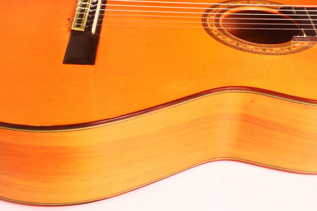Nahaufnahme einer Flamenco-Gitarre von José M Palmero aus dem Jahr 2023, bei der die Saiten, der Steg, das Schallloch und der polierte Holzkorpus mit einer warmen orange-braunen Lackierung besonders hervorgehoben werden. Nahaufnahme einer Flamenco-Gitarre von José M Palmero aus dem Jahr 2023, bei der die Saiten, der Steg, das Schallloch und der polierte Holzkorpus mit einer warmen orange-braunen Lackierung besonders hervorgehoben werden.
