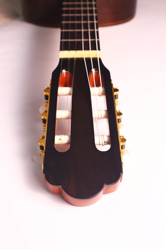 Nahaufnahme der Kopfplatte der Vicente Carrillo 1998 Torres Klassische Gitarre mit Stimmwirbeln, Saiten und dunkler Holzoberfläche vor einem hellen Hintergrund. Nahaufnahme der Kopfplatte der Vicente Carrillo 1998 Torres Klassische Gitarre mit Stimmwirbeln, Saiten und dunkler Holzoberfläche vor einem hellen Hintergrund.