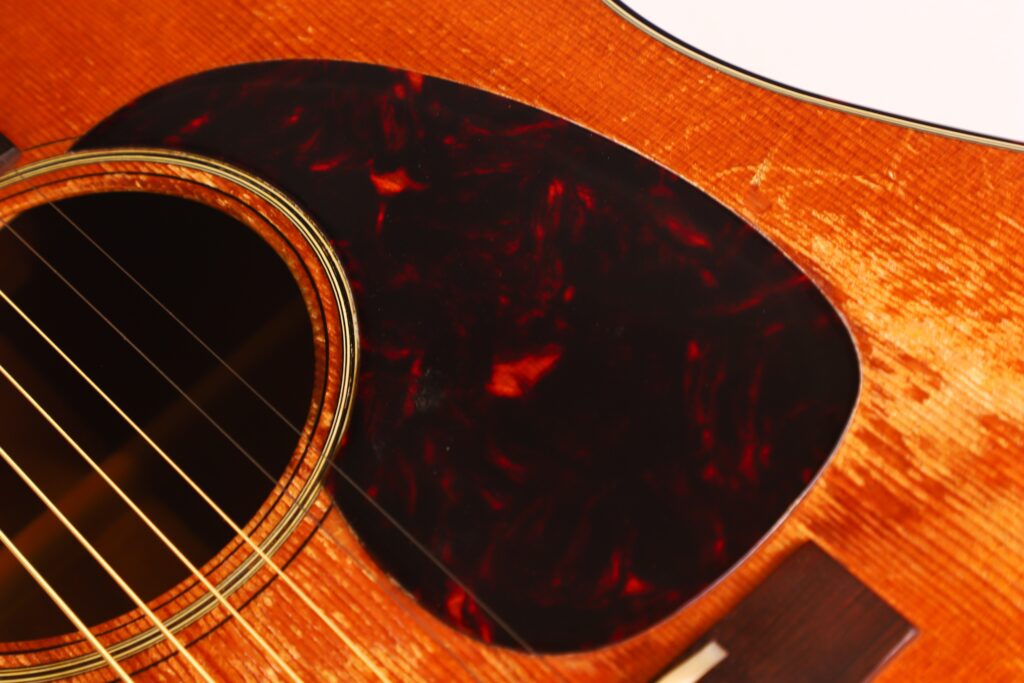 Nahaufnahme einer Martin D-21 1965 Akustik Gitarre mit Schallloch, goldenen Saiten, dunkelrotem Schildpatt-Schlagbrett und Holzmaserung auf dem Korpus. Nahaufnahme einer Martin D-21 1965 Akustik Gitarre mit Schallloch, goldenen Saiten, dunkelrotem Schildpatt-Schlagbrett und Holzmaserung auf dem Korpus.