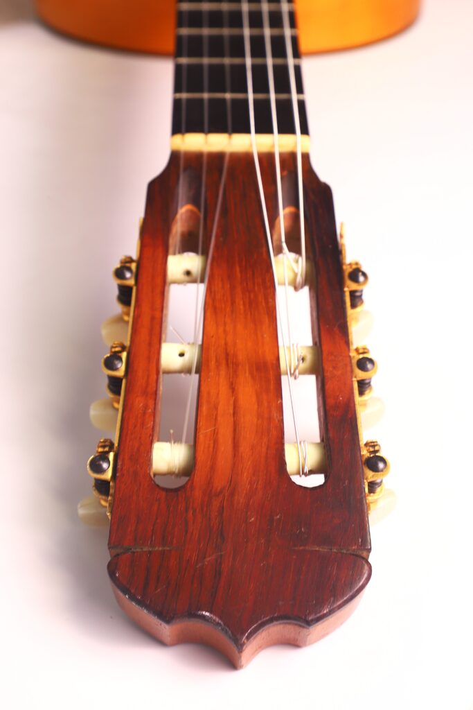 Nahaufnahme der Kopfplatte der Flamenco-Gitarre von Jose Ramirez aus dem Jahr 1955 mit sechs Saiten, hölzernen Stimmwirbeln und einer polierten Holzoberfläche vor einem schlichten, hellen Hintergrund. Nahaufnahme der Kopfplatte der Flamenco-Gitarre von Jose Ramirez aus dem Jahr 1955 mit sechs Saiten, hölzernen Stimmwirbeln und einer polierten Holzoberfläche vor einem schlichten, hellen Hintergrund.