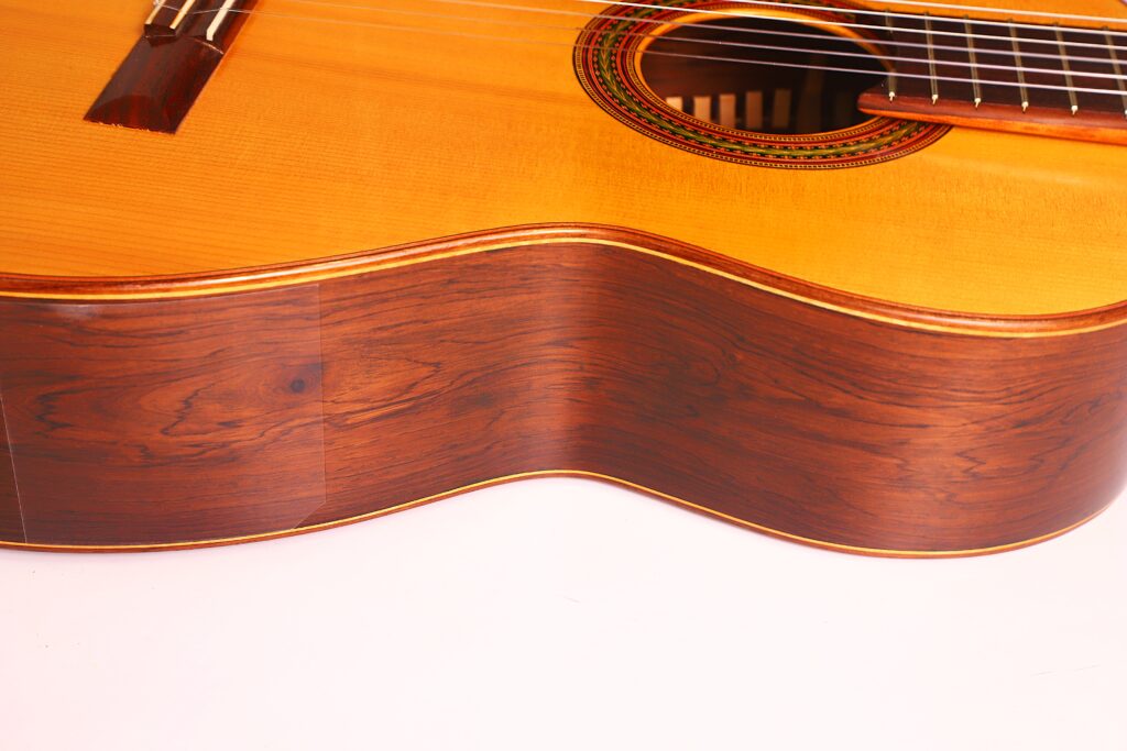 Nahaufnahme einer „Carl Hermann Schäfer – Nicolaus Wollf 2012“ Klassischen Gitarre, die den glänzenden Holzkorpus und die dekorative Einlage am Schallloch vor weißem Hintergrund hervorhebt. Nahaufnahme einer „Carl Hermann Schäfer – Nicolaus Wollf 2012“ Klassischen Gitarre, die den glänzenden Holzkorpus und die dekorative Einlage am Schallloch vor weißem Hintergrund hervorhebt.