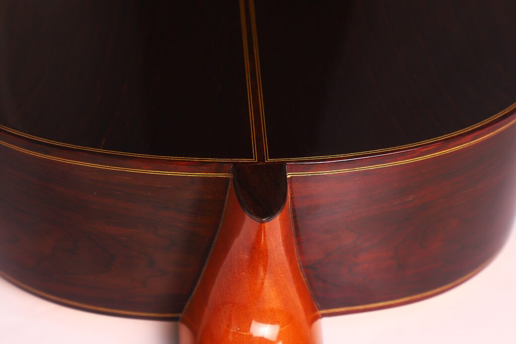 Nahaufnahme des Bodens und des Halses einer Vicente Carrillo 1998 Torres Klassische Gitarre. Hervorzuheben sind das polierte dunkle Holz mit feiner Maserung, das gelbe Binding und die fachmännische Verarbeitung. Nahaufnahme des Bodens und des Halses einer Vicente Carrillo 1998 Torres Klassische Gitarre. Hervorzuheben sind das polierte dunkle Holz mit feiner Maserung, das gelbe Binding und die fachmännische Verarbeitung.