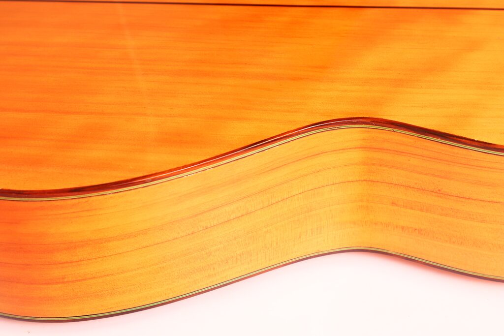 Nahaufnahme der Seite und Rückseite der José M Palmero 2023 Flamenco-Gitarre, die ihre natürliche Holzmaserung und ihre glänzende Lackierung im hellen Licht zur Geltung bringt. Nahaufnahme der Seite und Rückseite der José M Palmero 2023 Flamenco-Gitarre, die ihre natürliche Holzmaserung und ihre glänzende Lackierung im hellen Licht zur Geltung bringt.