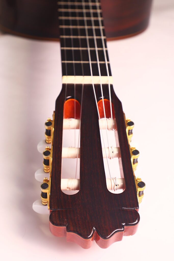 Nahaufnahme der Kopfplatte und des Halses einer Juan Miguel Gonzalez 2006 Klassische Gitarre. Hervorzuheben sind die Stimmwirbel, die Saiten und die dunkle Holzoberfläche, aufgenommen vor einem sanft beleuchteten Hintergrund. Nahaufnahme der Kopfplatte und des Halses einer Juan Miguel Gonzalez 2006 Klassische Gitarre. Hervorzuheben sind die Stimmwirbel, die Saiten und die dunkle Holzoberfläche, aufgenommen vor einem sanft beleuchteten Hintergrund.