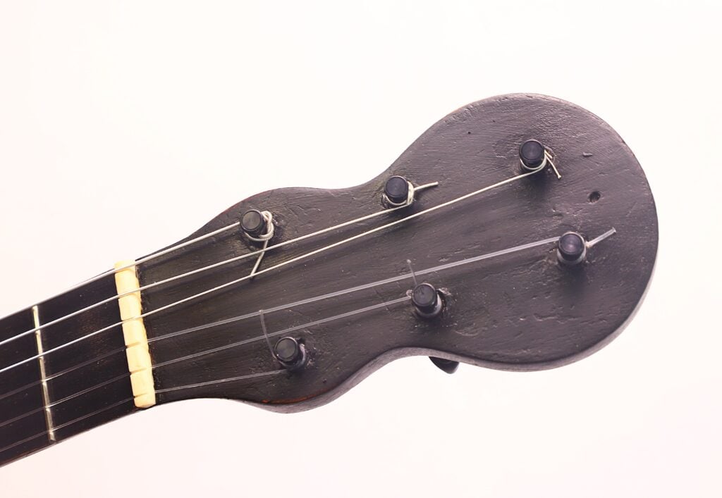 Nahaufnahme des Kopfes einer italienischen Romantikgitarre von 1860 mit Stimmwirbeln und Saiten, dargestellt in dunkler Holzoptik vor einem schlichten weißen Hintergrund. Nahaufnahme des Kopfes einer italienischen Romantikgitarre von 1860 mit Stimmwirbeln und Saiten, dargestellt in dunkler Holzoptik vor einem schlichten weißen Hintergrund.