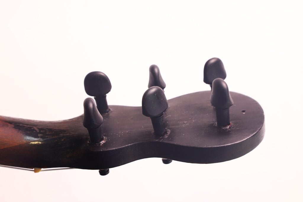 Nahaufnahme des Kopfes der „Italienischen Romantikgitarre 1860“ mit fünf schwarzen Stimmwirbeln vor einem schlichten weißen Hintergrund. Nahaufnahme des Kopfes der „Italienischen Romantikgitarre 1860“ mit fünf schwarzen Stimmwirbeln vor einem schlichten weißen Hintergrund.