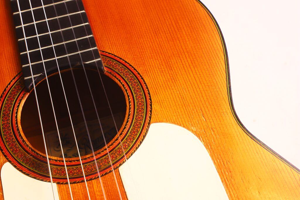 Nahaufnahme des Korpus und des Schalllochs der Flamenco-Gitarre von Jose Ramirez aus dem Jahr 1955. Hervorzuheben sind die detaillierte Holzmaserung, die verzierte Rosette sowie ein Teil der Saiten und des Griffbretts vor einem weißen Hintergrund. Nahaufnahme des Korpus und des Schalllochs der Flamenco-Gitarre von Jose Ramirez aus dem Jahr 1955. Hervorzuheben sind die detaillierte Holzmaserung, die verzierte Rosette sowie ein Teil der Saiten und des Griffbretts vor einem weißen Hintergrund.
