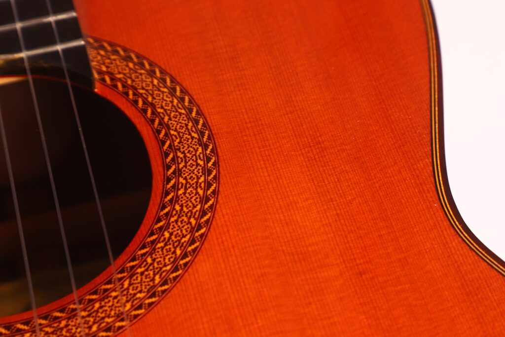 Nahaufnahme der Juan Miguel Gonzalez 2006 Klassische Gitarre, die die Saiten, das Schallloch und das komplizierte Rosettenmuster auf dem Holzkorpus hervorhebt. Nahaufnahme der Juan Miguel Gonzalez 2006 Klassische Gitarre, die die Saiten, das Schallloch und das komplizierte Rosettenmuster auf dem Holzkorpus hervorhebt.