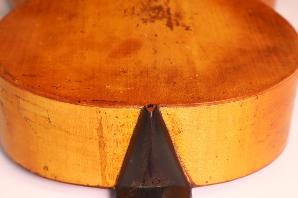 Nahaufnahme der Rückseite und der Unterkante einer „Italienischen Romantikgitarre 1860“, wobei die Verbindungsstelle zwischen Hals und Korpus hervorgehoben ist. Das hellbraune Holz weist eine sichtbare Maserung und einige Gebrauchsspuren auf. Nahaufnahme der Rückseite und der Unterkante einer „Italienischen Romantikgitarre 1860“, wobei die Verbindungsstelle zwischen Hals und Korpus hervorgehoben ist. Das hellbraune Holz weist eine sichtbare Maserung und einige Gebrauchsspuren auf.