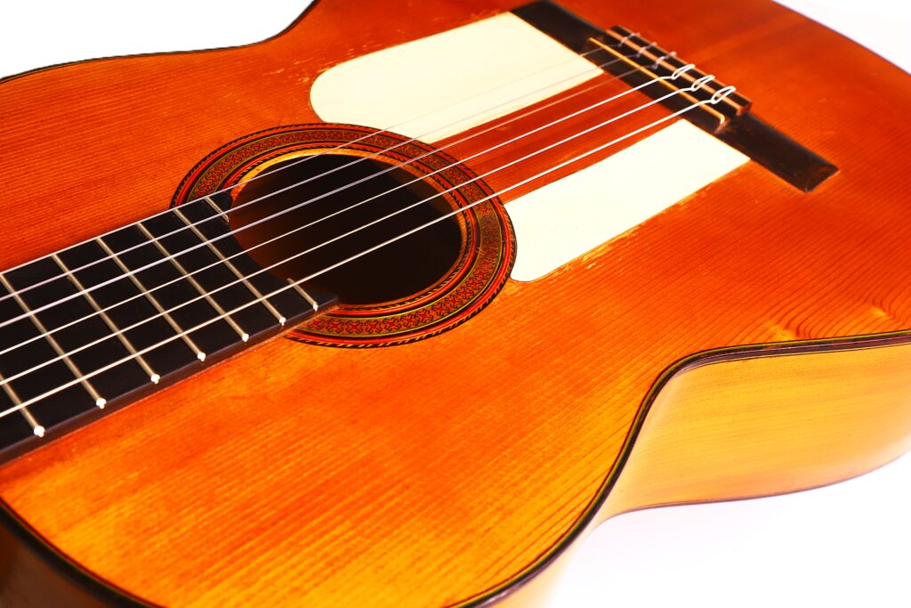 Eine Nahaufnahme der Flamenco-Gitarre von Jose Ramirez aus dem Jahr 1955 zeigt den Holzkorpus, die Saiten, das mit einer Rosette verzierte Schallloch und einen Teil des Griffbretts vor einem weißen Hintergrund. Eine Nahaufnahme der Flamenco-Gitarre von Jose Ramirez aus dem Jahr 1955 zeigt den Holzkorpus, die Saiten, das mit einer Rosette verzierte Schallloch und einen Teil des Griffbretts vor einem weißen Hintergrund.