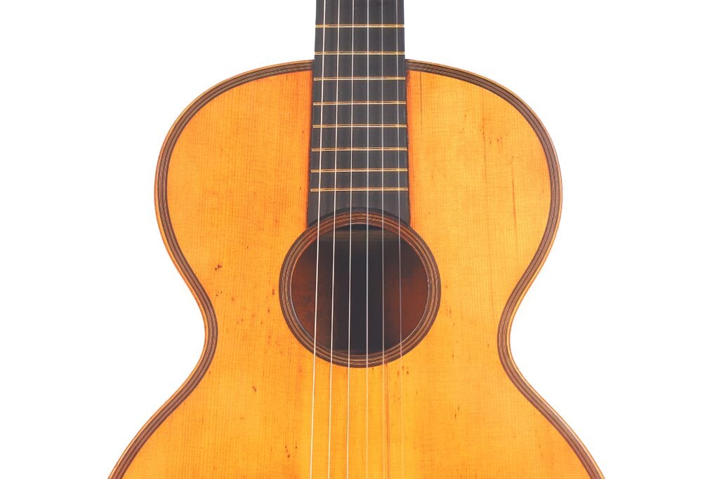 Nahaufnahme des Korpus und des Halses der Romantikgitarre Markneukirchen 1880 mit Holzoberfläche, Saiten und rundem Schallloch vor einem weißen Hintergrund. Nahaufnahme des Korpus und des Halses der Romantikgitarre Markneukirchen 1880 mit Holzoberfläche, Saiten und rundem Schallloch vor einem weißen Hintergrund.