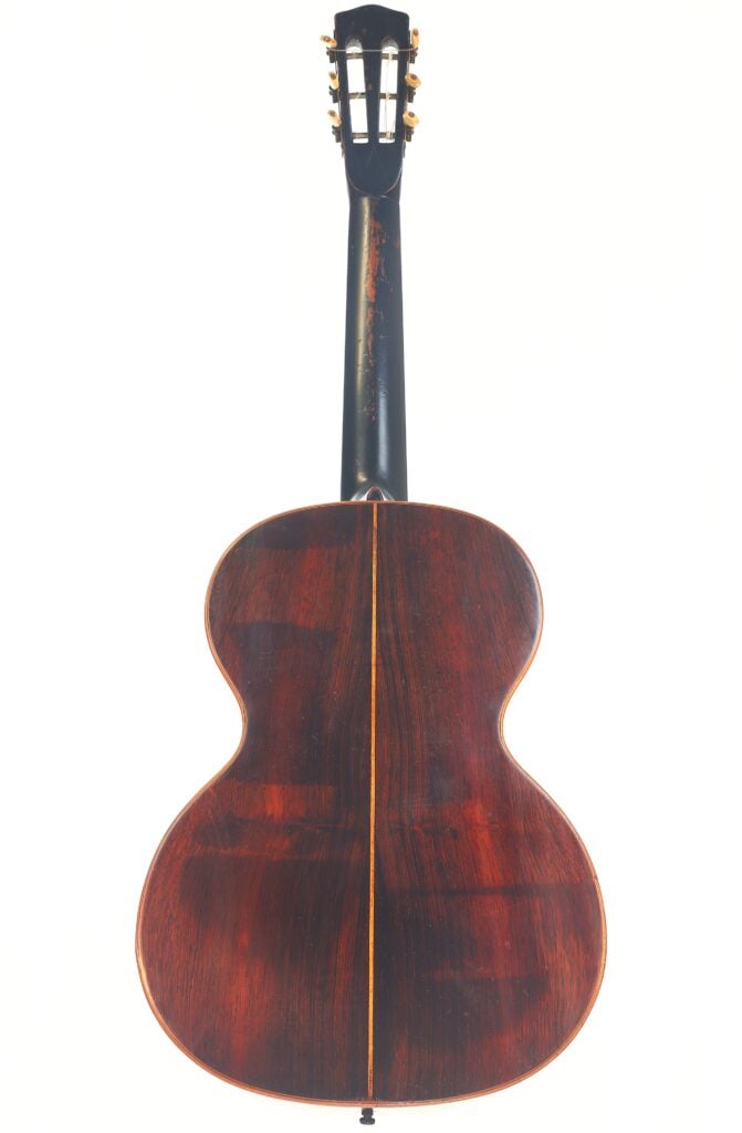 Die Markneukirchen 1880 Romantikgitarre wird von hinten gezeigt. Sie hat dunkles, poliertes Holz mit einem vertikalen, hellen Mittelstreifen und einen schwarzen Hals mit Stimmwirbeln. Die Markneukirchen 1880 Romantikgitarre wird von hinten gezeigt. Sie hat dunkles, poliertes Holz mit einem vertikalen, hellen Mittelstreifen und einen schwarzen Hals mit Stimmwirbeln.