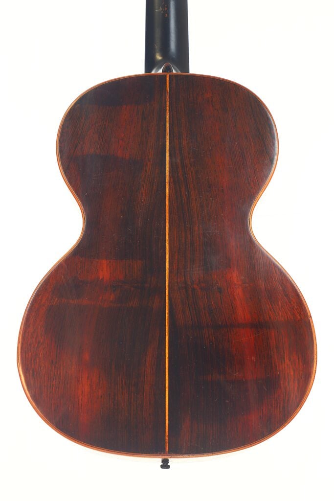 Die Abbildung zeigt die Rückseite der Markneukirchen 1880 Romantikgitarre, die sich durch eine reiche dunkle Holzmaserung, eine detaillierte zentrale Einlage, eine polierte rotbraune Oberfläche und elegante Kurven auszeichnet. Die Abbildung zeigt die Rückseite der Markneukirchen 1880 Romantikgitarre, die sich durch eine reiche dunkle Holzmaserung, eine detaillierte zentrale Einlage, eine polierte rotbraune Oberfläche und elegante Kurven auszeichnet.