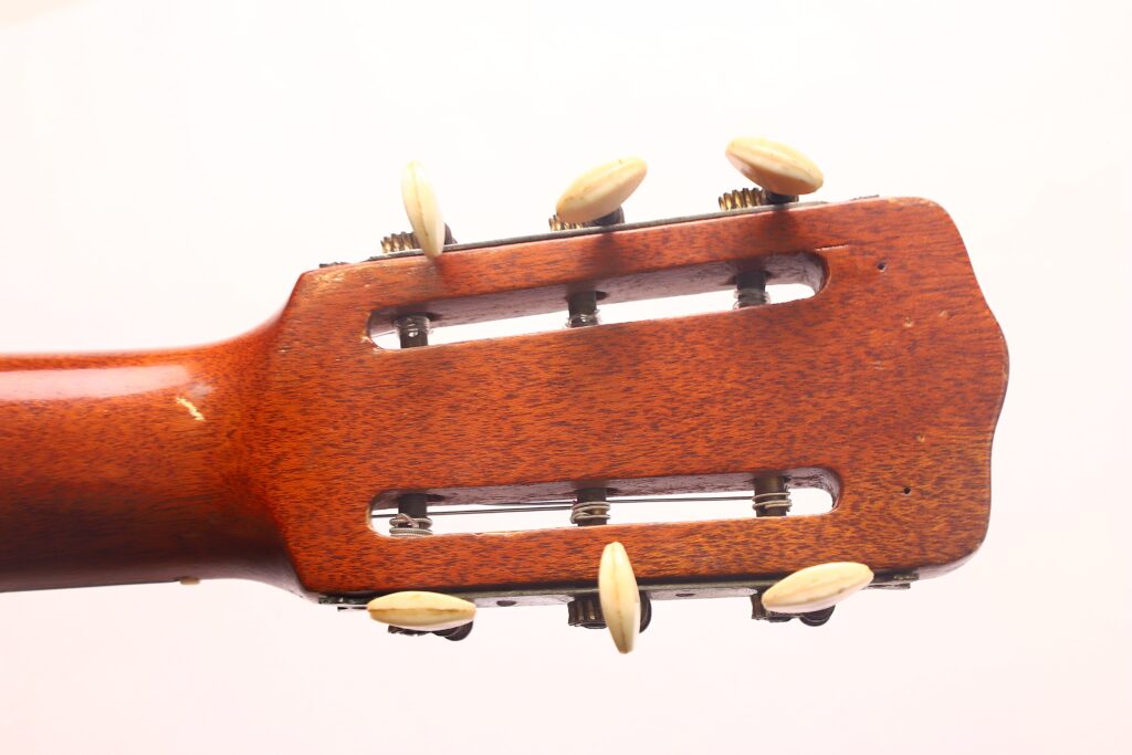 Nahaufnahme einer Ricardo Sanchis Nacher 1940 Flamenco-Gitarre mit hölzerner Kopfplatte, sechs weißen Stimmwirbeln (drei pro Seite) und zwei verlängerten Schlitzen für die Saiten. Nahaufnahme einer Ricardo Sanchis Nacher 1940 Flamenco-Gitarre mit hölzerner Kopfplatte, sechs weißen Stimmwirbeln (drei pro Seite) und zwei verlängerten Schlitzen für die Saiten.