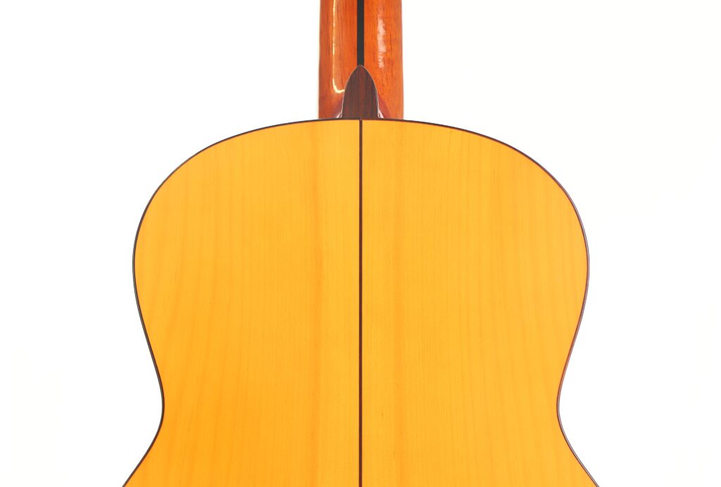 Nahaufnahme der Rückseite einer Flamenco-Gitarre von Antonio Bernal aus dem Jahr 2009, die helles Holz mit einer dunklen Mittelnaht und einem Teil des Halses zeigt, vor einem weißen Hintergrund. Nahaufnahme der Rückseite einer Flamenco-Gitarre von Antonio Bernal aus dem Jahr 2009, die helles Holz mit einer dunklen Mittelnaht und einem Teil des Halses zeigt, vor einem weißen Hintergrund.
