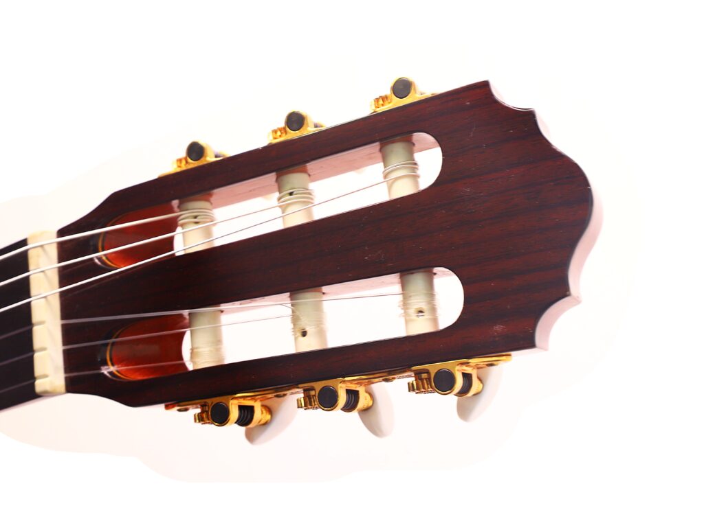 Nahaufnahme des Kopfes einer Flamenco-Gitarre von Antonio Bernal aus dem Jahr 2009 mit hölzernen Stimmwirbeln, weißen Saiten und goldenen Stimmmechaniken vor weißem Hintergrund. Nahaufnahme des Kopfes einer Flamenco-Gitarre von Antonio Bernal aus dem Jahr 2009 mit hölzernen Stimmwirbeln, weißen Saiten und goldenen Stimmmechaniken vor weißem Hintergrund.