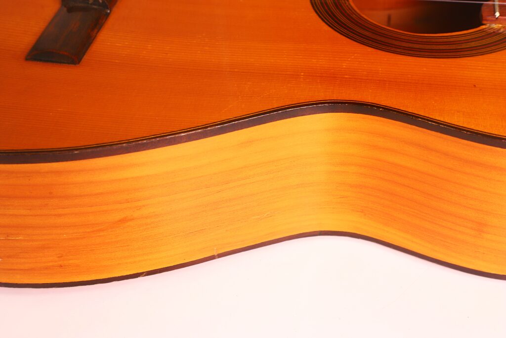 Nahaufnahme der Ricardo Sanchis Nacher 1940 Flamenco Gitarre, die die natürliche Holzmaserung, den gewölbten Korpus und die dunkle Zierleiste vor einem weißen Hintergrund hervorhebt. Nahaufnahme der Ricardo Sanchis Nacher 1940 Flamenco Gitarre, die die natürliche Holzmaserung, den gewölbten Korpus und die dunkle Zierleiste vor einem weißen Hintergrund hervorhebt.