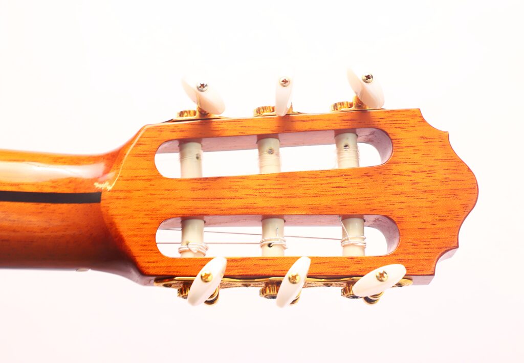 Nahaufnahme des Kopfes einer Flamenco-Gitarre von Antonio Bernal aus dem Jahr 2009 mit Holzoberfläche, weißen Stimmwirbeln und sichtbaren Saiten vor einem schlichten weißen Hintergrund. Nahaufnahme des Kopfes einer Flamenco-Gitarre von Antonio Bernal aus dem Jahr 2009 mit Holzoberfläche, weißen Stimmwirbeln und sichtbaren Saiten vor einem schlichten weißen Hintergrund.
