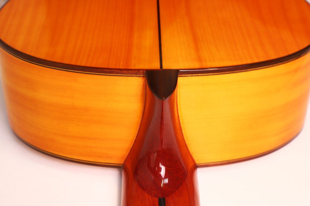 Nahaufnahme des Halsansatzes einer Flamenco-Gitarre von Antonio Bernal aus dem Jahr 2009, die vor weißem Hintergrund die glänzende Holzoberfläche und die sanften Rundungen hervorhebt. Nahaufnahme des Halsansatzes einer Flamenco-Gitarre von Antonio Bernal aus dem Jahr 2009, die vor weißem Hintergrund die glänzende Holzoberfläche und die sanften Rundungen hervorhebt.
