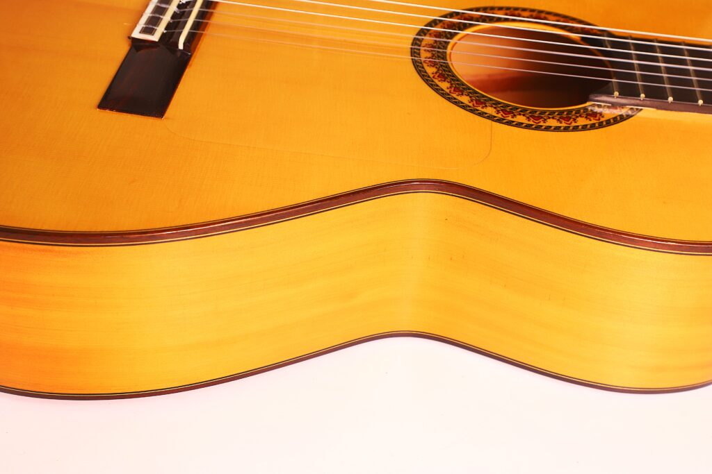 Nahaufnahme des Korpus einer Flamenco-Gitarre von Antonio Bernal aus dem Jahr 2009, die vor einem hellen Hintergrund die geschwungenen Holzformen, die Saiten und die dekorative Rosette um das Schallloch herum hervorhebt. Nahaufnahme des Korpus einer Flamenco-Gitarre von Antonio Bernal aus dem Jahr 2009, die vor einem hellen Hintergrund die geschwungenen Holzformen, die Saiten und die dekorative Rosette um das Schallloch herum hervorhebt.