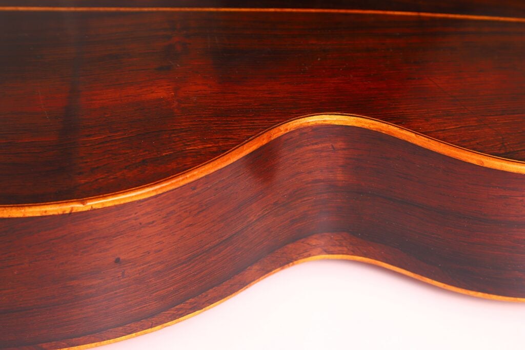 Nahaufnahme der Markneukirchen 1880 Romantikgitarre, die ihre elegant geschwungene Holzseite, die polierte braune Maserung und die feine Handwerkskunst zeigt. Nahaufnahme der Markneukirchen 1880 Romantikgitarre, die ihre elegant geschwungene Holzseite, die polierte braune Maserung und die feine Handwerkskunst zeigt.