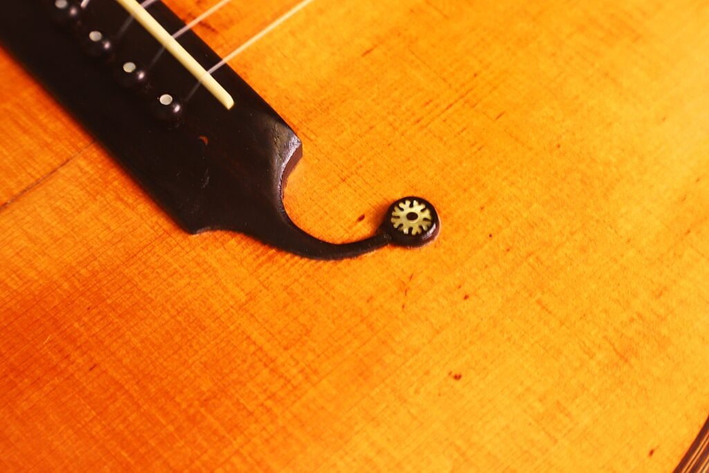 Nahaufnahme einer Romantikgitarre von Markneukirchen aus dem Jahr 1880, bei der der Steg, die dekorative Einlage und die Saiten auf der polierten orange-braunen Holzoberfläche hervorgehoben werden. Nahaufnahme einer Romantikgitarre von Markneukirchen aus dem Jahr 1880, bei der der Steg, die dekorative Einlage und die Saiten auf der polierten orange-braunen Holzoberfläche hervorgehoben werden.