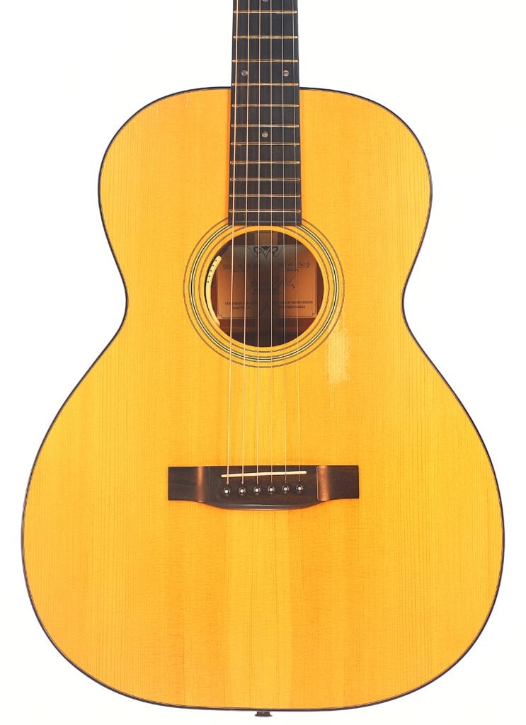 Eine Nahaufnahme der Rozawood 000 12-18-HM Akustik Gitarre zeigt den Korpus, die Saiten, das Schallloch und den Hals vor einem weißen Hintergrund. Die Gitarre hat eine helle Holzoberfläche und ein klassisches, einfaches Design. Eine Nahaufnahme der Rozawood 000 12-18-HM Akustik Gitarre zeigt den Korpus, die Saiten, das Schallloch und den Hals vor einem weißen Hintergrund. Die Gitarre hat eine helle Holzoberfläche und ein klassisches, einfaches Design.