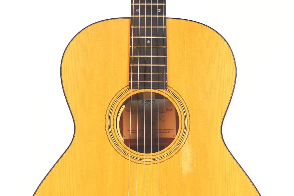Eine Nahaufnahme des Korpus und des Halses der Rozawood 000 12-18-HM Akustik Gitarre, die die Holzoberfläche, die Saiten und das Schallloch vor einem weißen Hintergrund hervorhebt. Eine Nahaufnahme des Korpus und des Halses der Rozawood 000 12-18-HM Akustik Gitarre, die die Holzoberfläche, die Saiten und das Schallloch vor einem weißen Hintergrund hervorhebt.