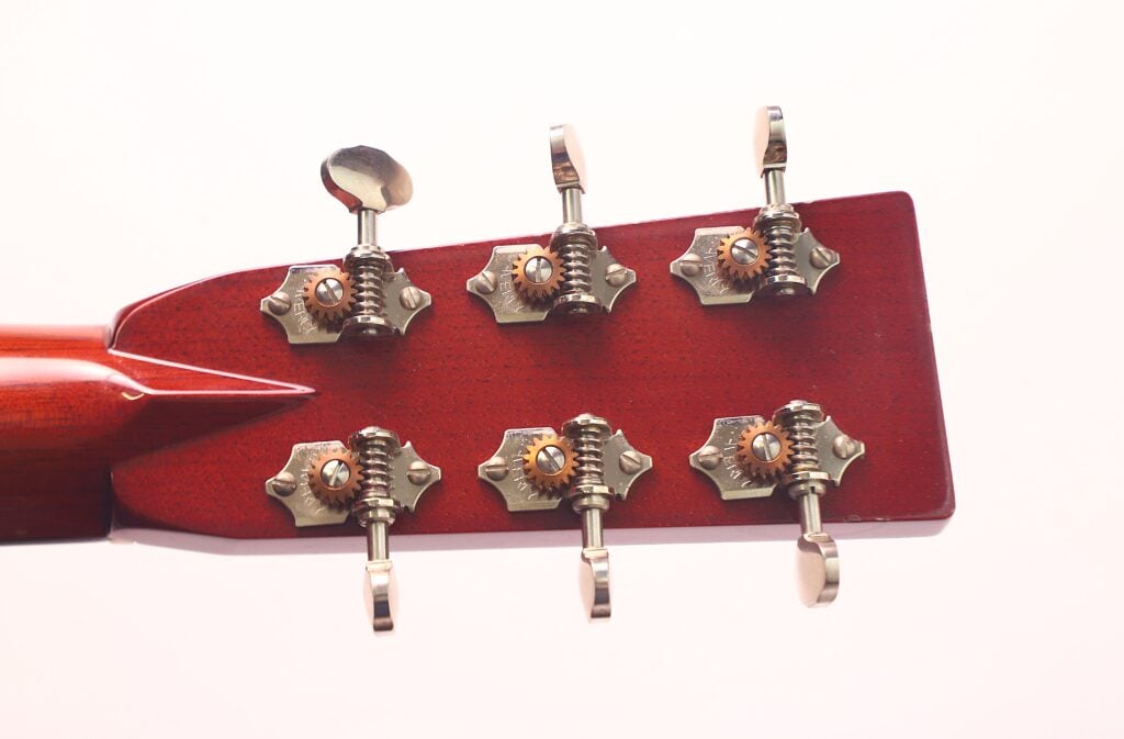 Nahaufnahme der Rückseite einer Rozawood 000 12-18-HM Akustik Gitarre mit sechs Metallstimmwirbeln. Die rötlich-braune Holzoberfläche kontrastiert mit silbern glänzenden Stimmmechaniken, Schrauben und Zahnrädern auf weißem Hintergrund. Nahaufnahme der Rückseite einer Rozawood 000 12-18-HM Akustik Gitarre mit sechs Metallstimmwirbeln. Die rötlich-braune Holzoberfläche kontrastiert mit silbern glänzenden Stimmmechaniken, Schrauben und Zahnrädern auf weißem Hintergrund.