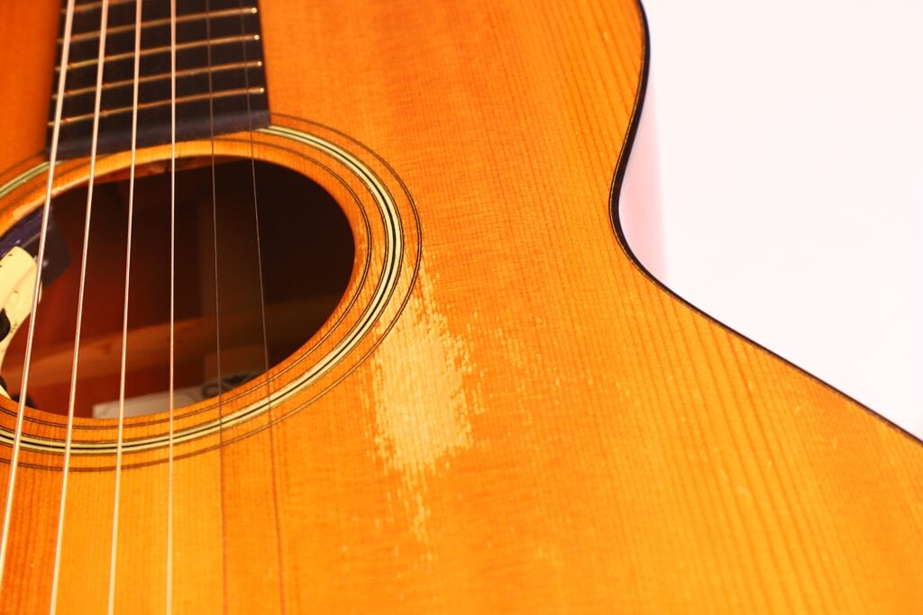 Nahaufnahme des Korpus einer Rozawood 000 12-18-HM Akustikgitarre, die das Schallloch, die Saiten und einen abgenutzten Holzbereich in der Nähe der Saiten vor einem weißen Hintergrund zeigt. Nahaufnahme des Korpus einer Rozawood 000 12-18-HM Akustikgitarre, die das Schallloch, die Saiten und einen abgenutzten Holzbereich in der Nähe der Saiten vor einem weißen Hintergrund zeigt.