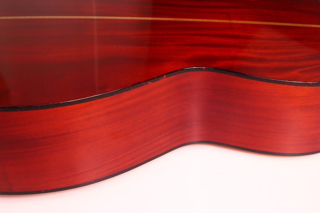 Nahaufnahme der Seite der Rozawood 000 12-18-HM Akustik Gitarre, die die glänzende, rötlich-braune Holzoberfläche mit sichtbaren Maserungen und einer schmalen schwarzen Umrandung zeigt. Nahaufnahme der Seite der Rozawood 000 12-18-HM Akustik Gitarre, die die glänzende, rötlich-braune Holzoberfläche mit sichtbaren Maserungen und einer schmalen schwarzen Umrandung zeigt.