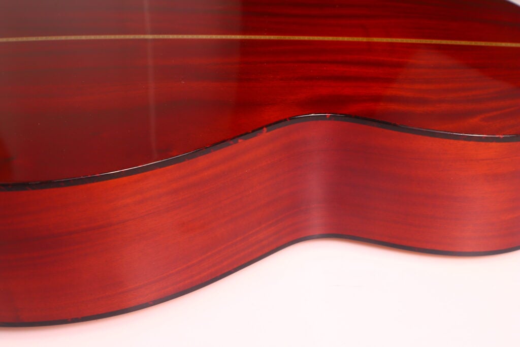 Nahaufnahme der glänzenden, rötlich-braunen Seite und Rückseite der Rozawood 000 12-18-HM Akustik Gitarre, die sanfte Kurven, Holzmaserung und dunkle Bindung vor einem hellen Hintergrund zeigt. Nahaufnahme der glänzenden, rötlich-braunen Seite und Rückseite der Rozawood 000 12-18-HM Akustik Gitarre, die sanfte Kurven, Holzmaserung und dunkle Bindung vor einem hellen Hintergrund zeigt.