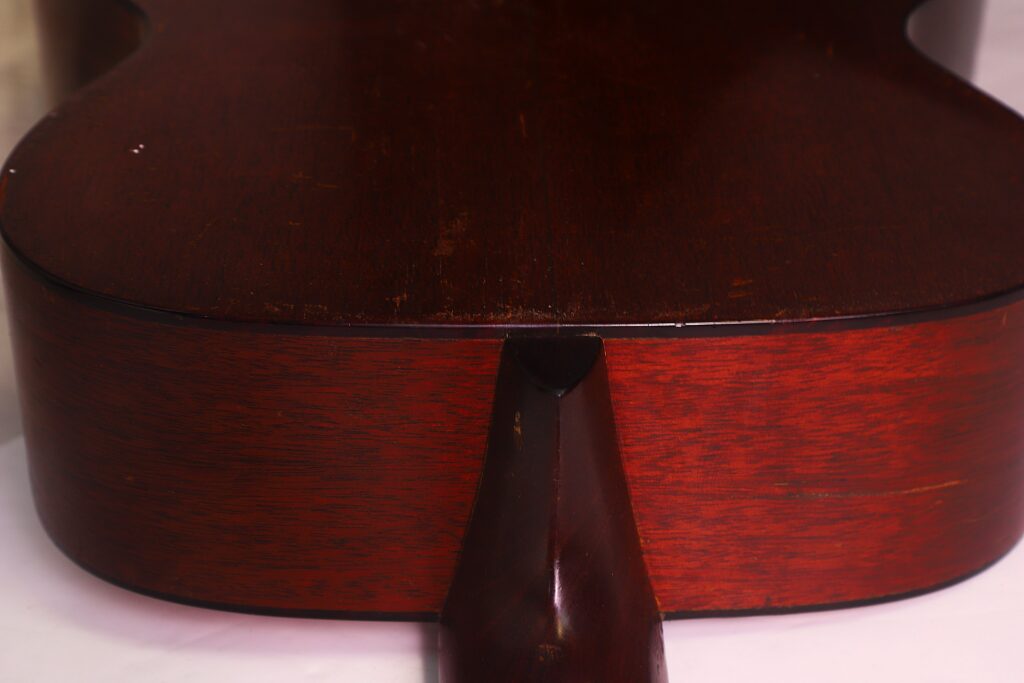 Nahaufnahme der Rückseite einer Martin 00-18 Akustikgitarre aus dem Jahr 1954, bei der der Halsansatz und die dunkelrotbraune Holzmaserung an der Verbindungsstelle zwischen Hals und Korpus besonders hervorgehoben sind. Nahaufnahme der Rückseite einer Martin 00-18 Akustikgitarre aus dem Jahr 1954, bei der der Halsansatz und die dunkelrotbraune Holzmaserung an der Verbindungsstelle zwischen Hals und Korpus besonders hervorgehoben sind.